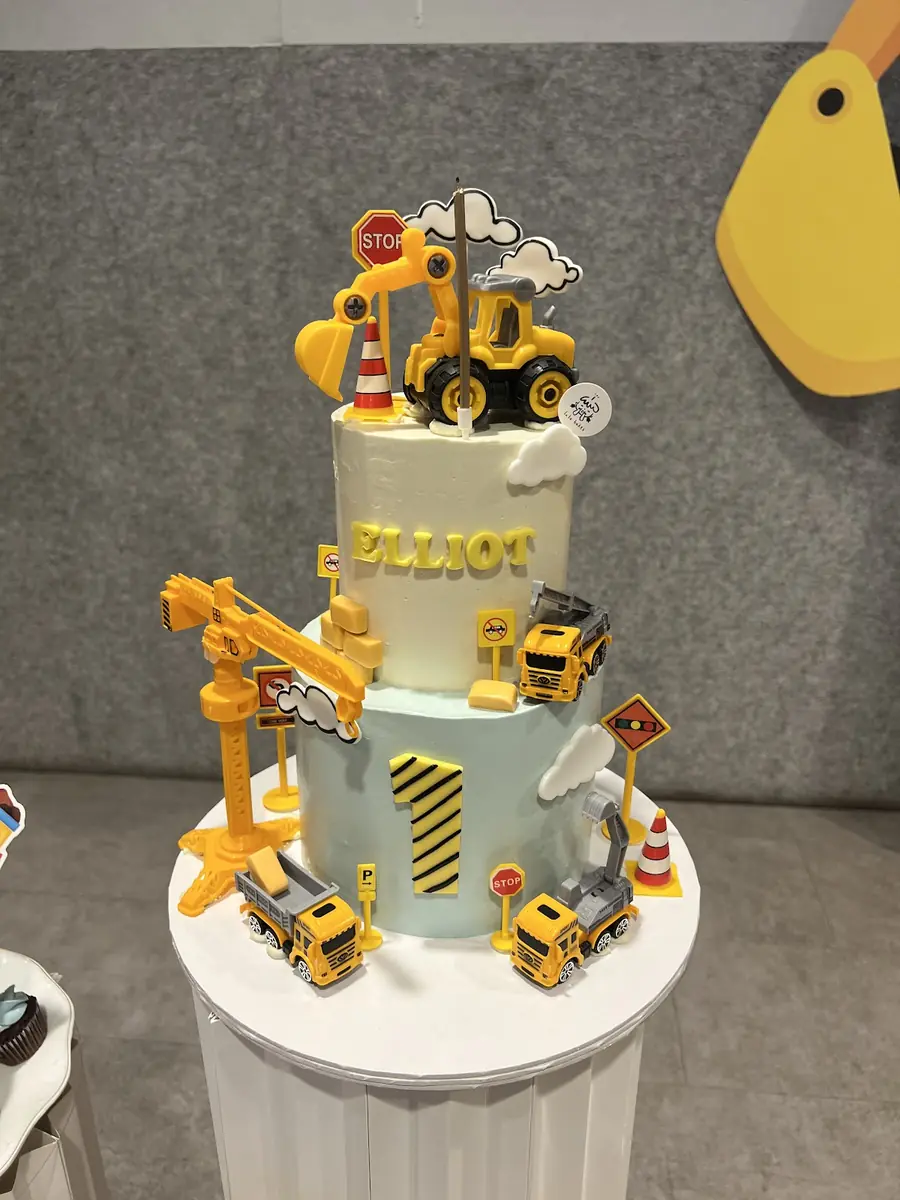 Two-tier construction-theme cake with toy diggers and a crane