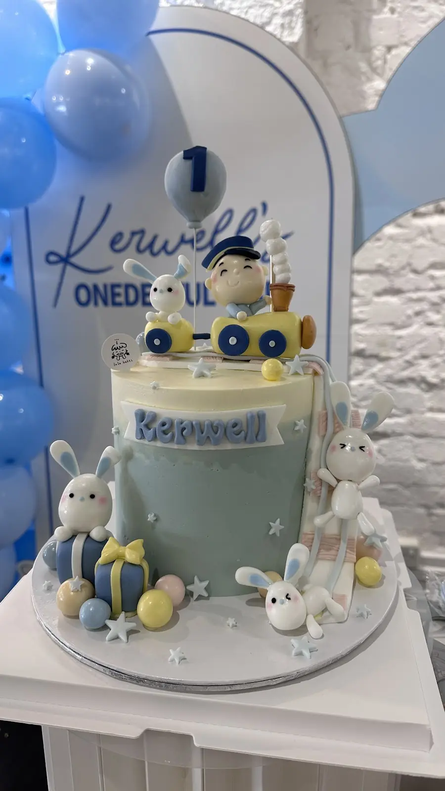 Blue first birthday cake with a teddy driving a toy car