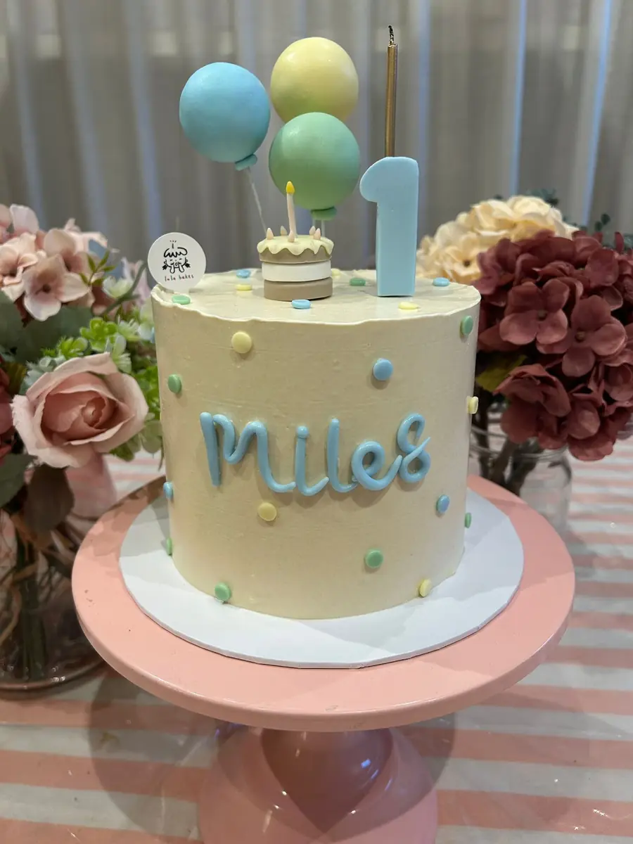 Pastel first birthday cake with balloon toppers